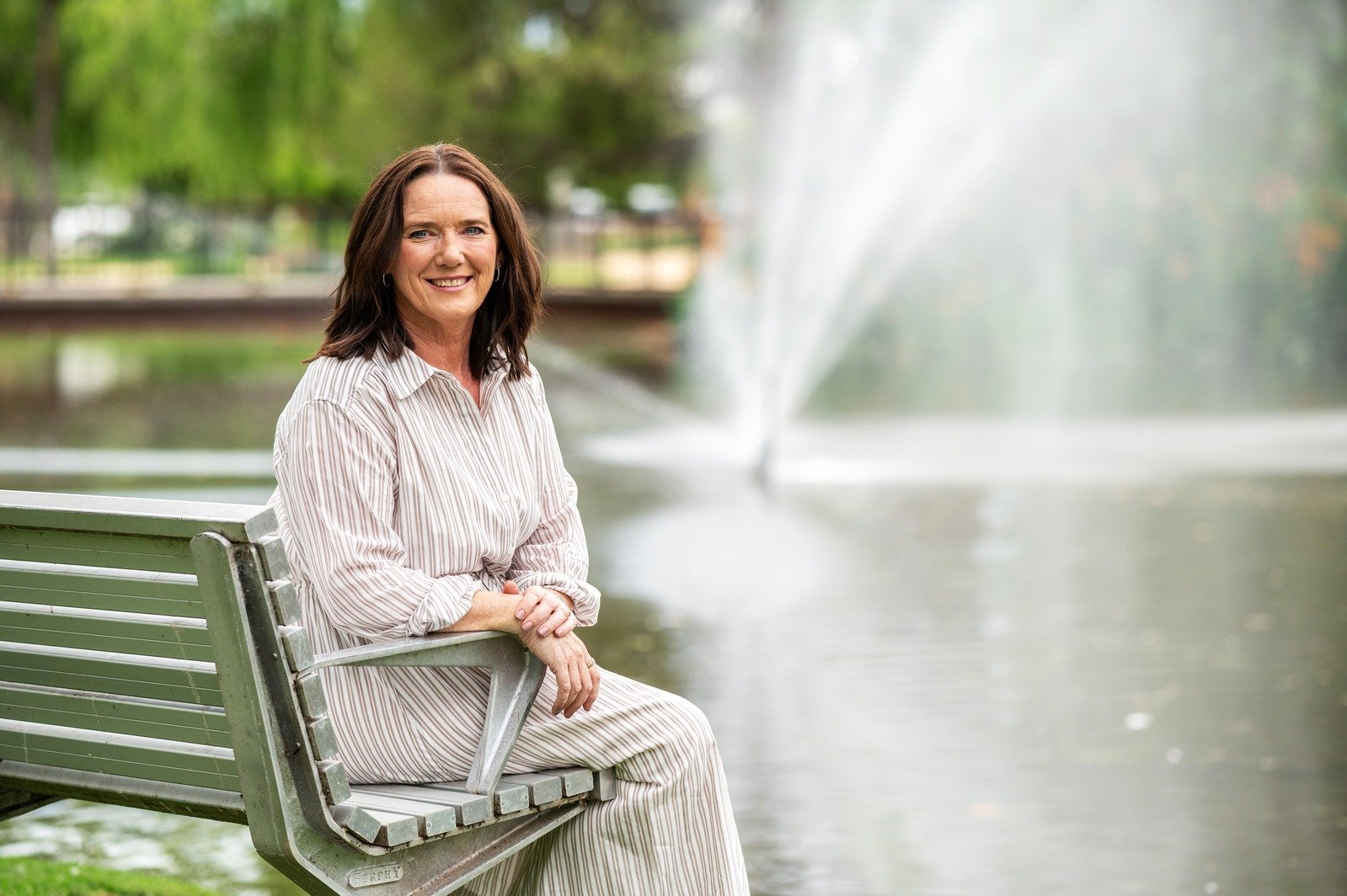 Louise Mace, holistic naturopath, seated peacefully by a fountain in a calming outdoor environment.